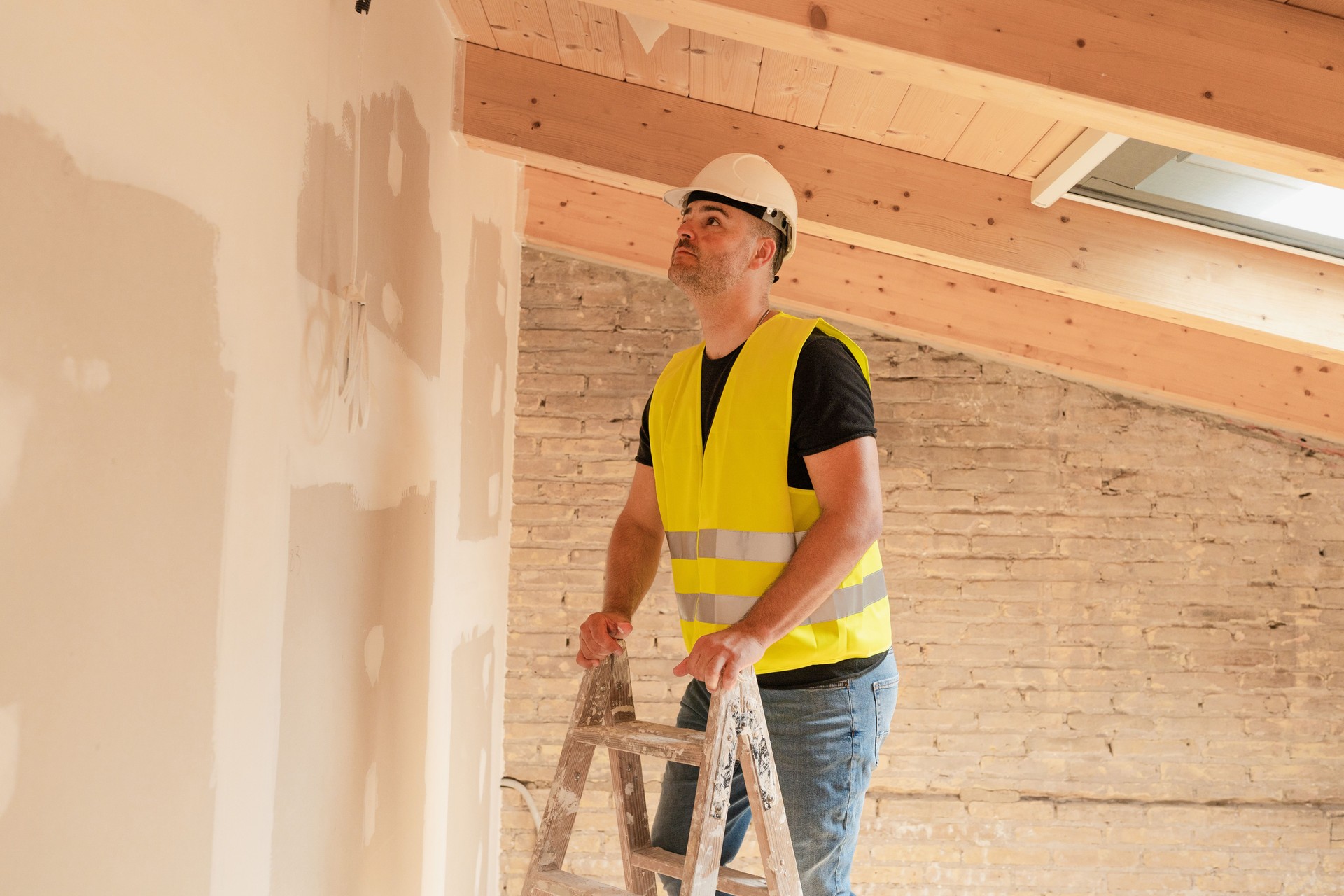 Male Construction worker wearing safety vest and helmet inspecting plaster work standing on a ladder